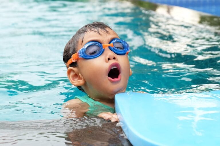 A happy child wearing colorful, leak-proof swimming goggles playing in a bright swimming pool