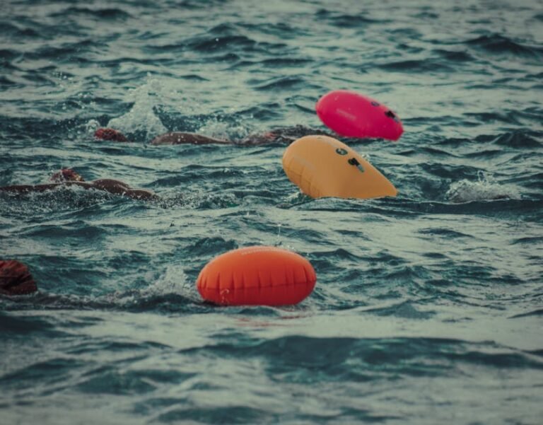 A triathlete swimming in the ocean towing a bright orange inflatable swim buoy for safety and visibility